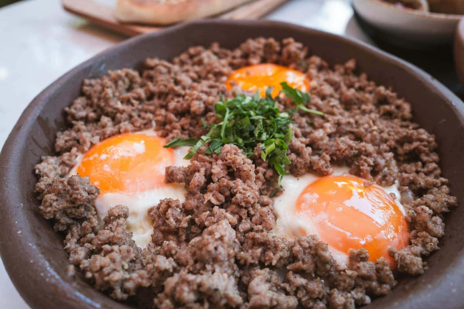 A flavorful skillet breakfast with sunny side up eggs and ground beef, garnished with fresh herbs.