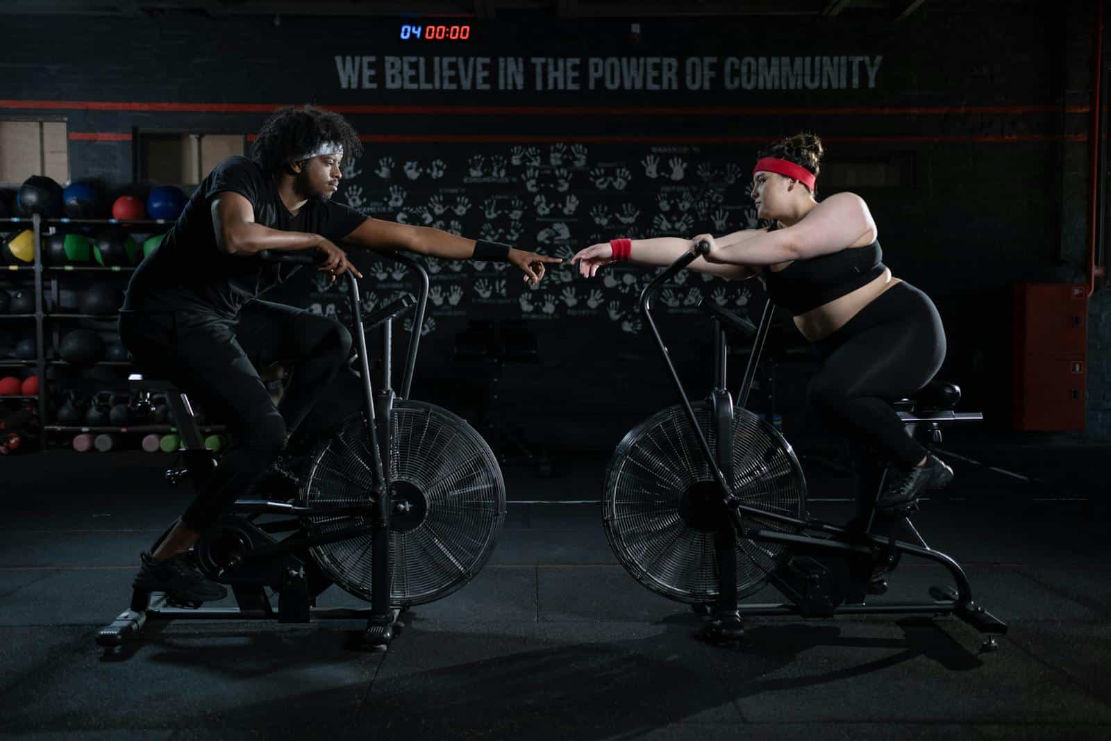 Two diverse individuals connect and motivate each other during a workout session on stationary bikes in a gym.