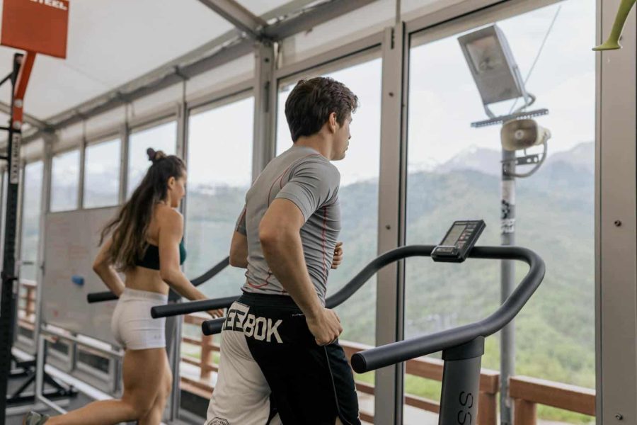 Two people running on treadmills in a gym with a mountain view, promoting fitness.