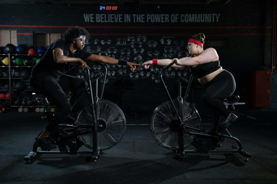 Two diverse individuals connect and motivate each other during a workout session on stationary bikes in a gym.